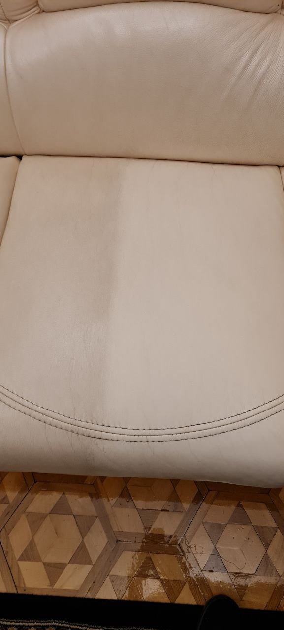 Fragment beżowej skórzanej sofy, widoczna różnica w czystości między wyczyszczoną a zabrudzoną częścią siedziska, na dole parkiet z geometrycznym wzorem.