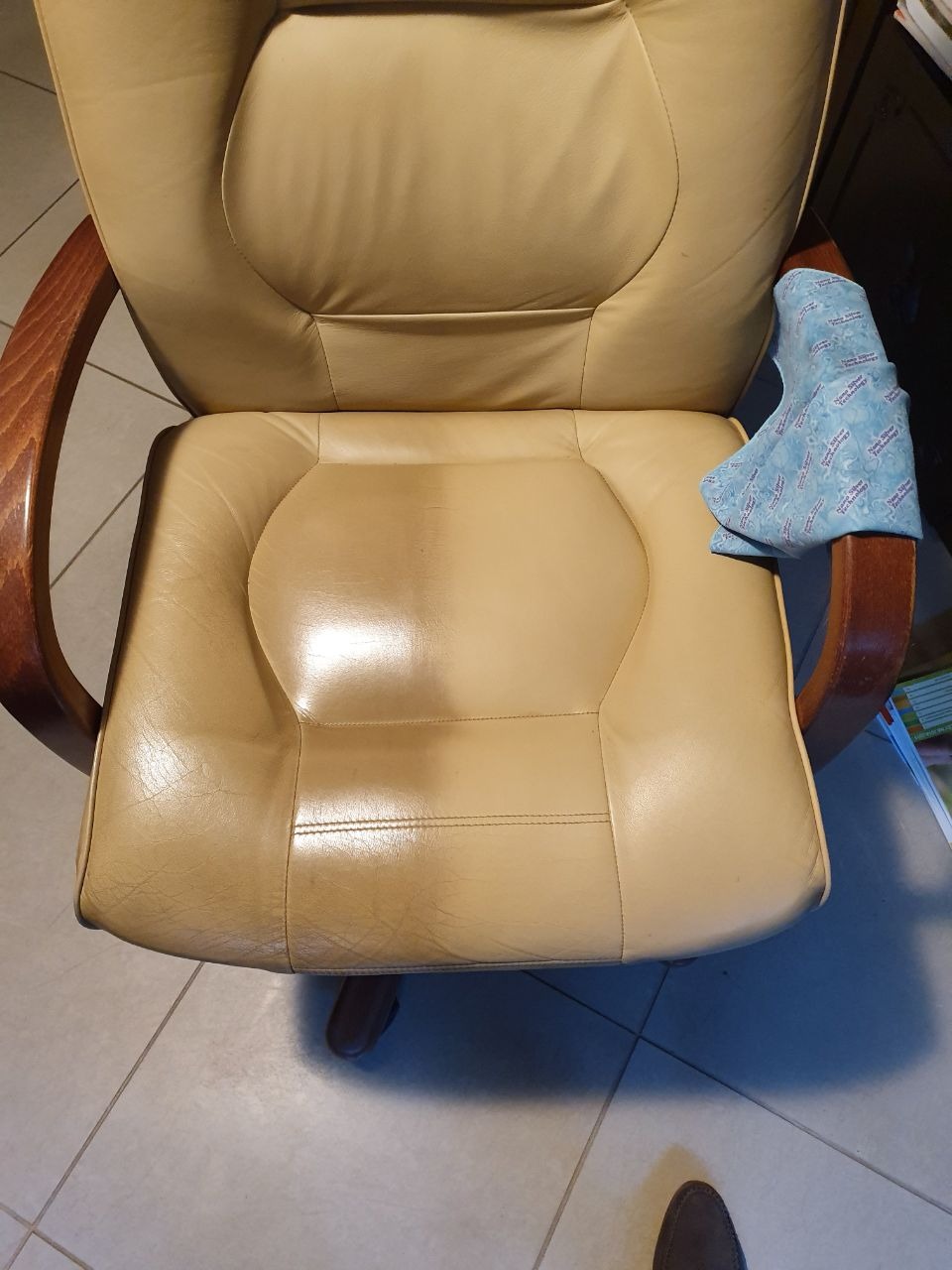 Czyszczenie skórzanego fotela biurowego: widoczna różnica w połysku po użyciu środka czyszczącego, niebieska ściereczka z mikrofibry oparta o podłokietnik.