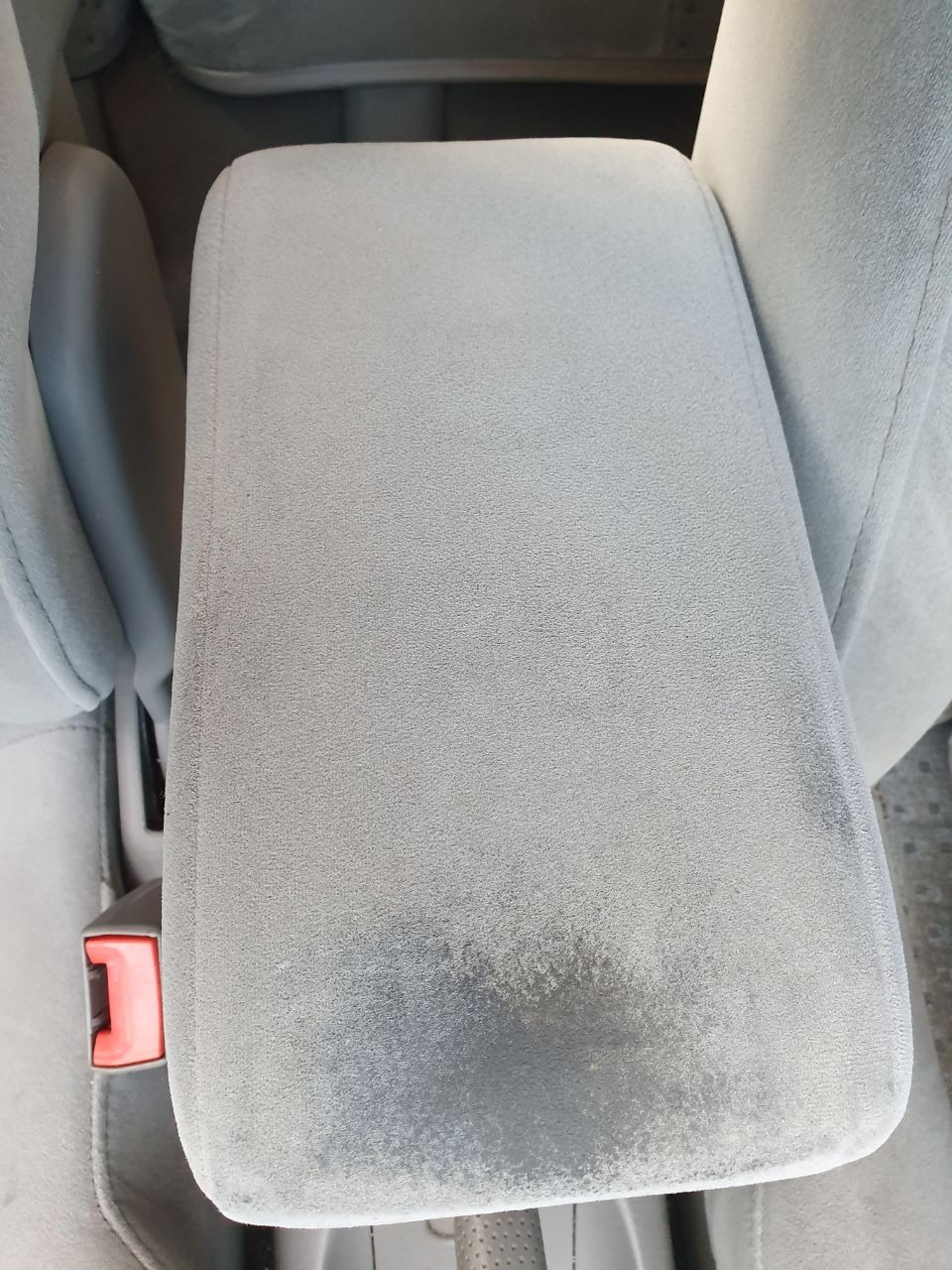 Tapicerowany podłokietnik samochodowy z widocznymi plamami i zabrudzeniami, wskazujący na potrzebę czyszczenia.