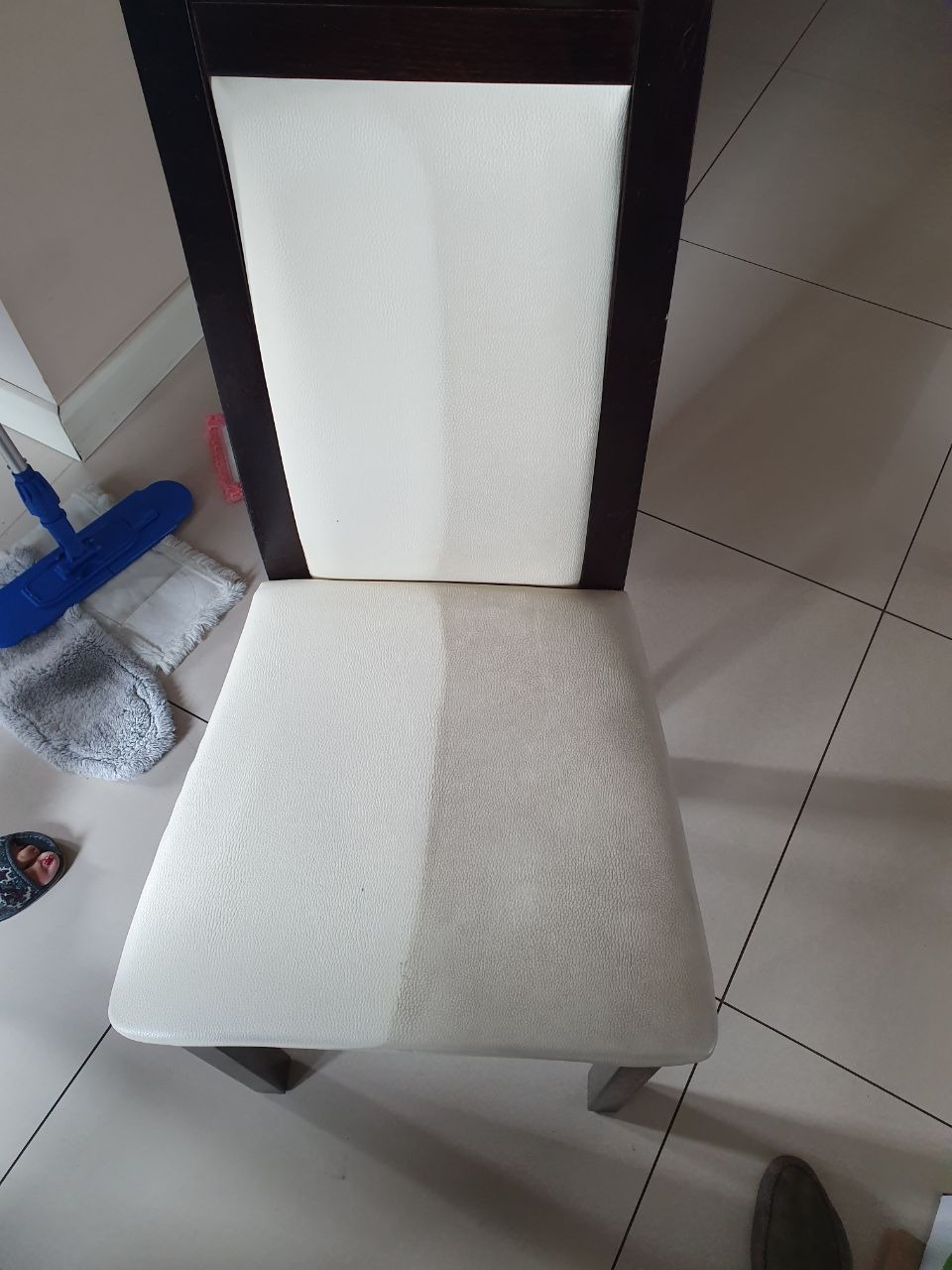 Krzesełko z tapicerką, widoczna różnica w czystości między wyczyszczoną a nie wyczyszczoną częścią siedziska, obok mop i ścierka.