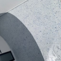 PROFESTON - Ściana i fragment sufitu wykończone jasnoszarymi płytkami z niebieskimi i szarymi drobnymi elementami, widoczne w narożniku fragmenty okna i listwy wykończeniowej.