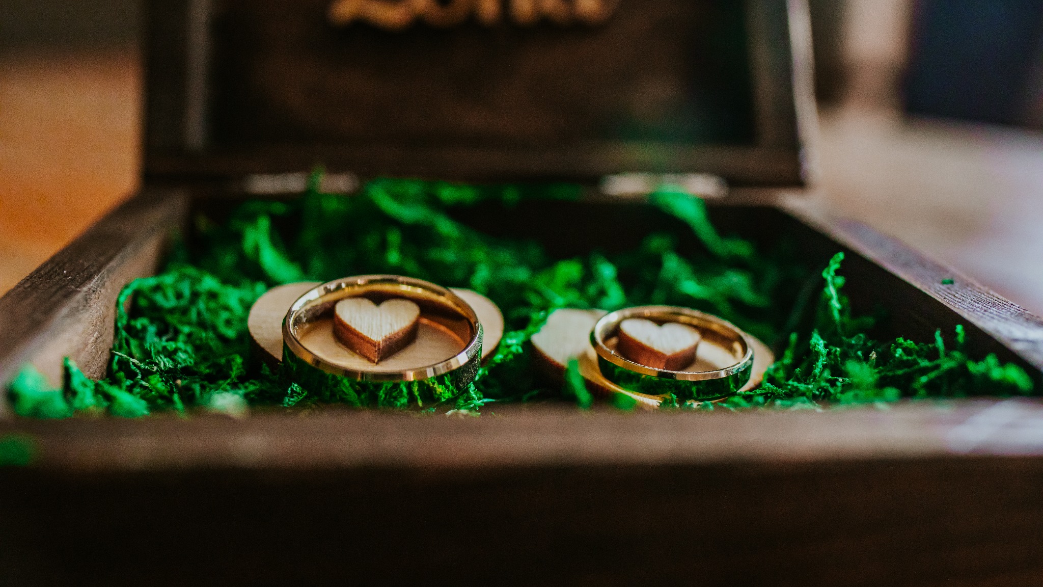 Dwa złote pierścionki ślubne z drewnianymi serduszkami w drewnianym pudełku wypełnionym zielonym mchem.