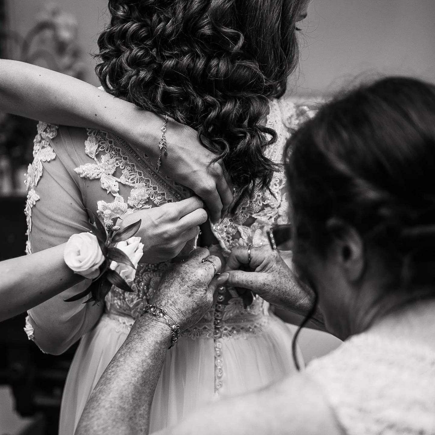 Czarno-białe zdjęcie z Iwierzyc przedstawia zapinanie sukni ślubnej panny młodej przez dwie osoby, widoczne detale koronki i kwiat na rękawie.