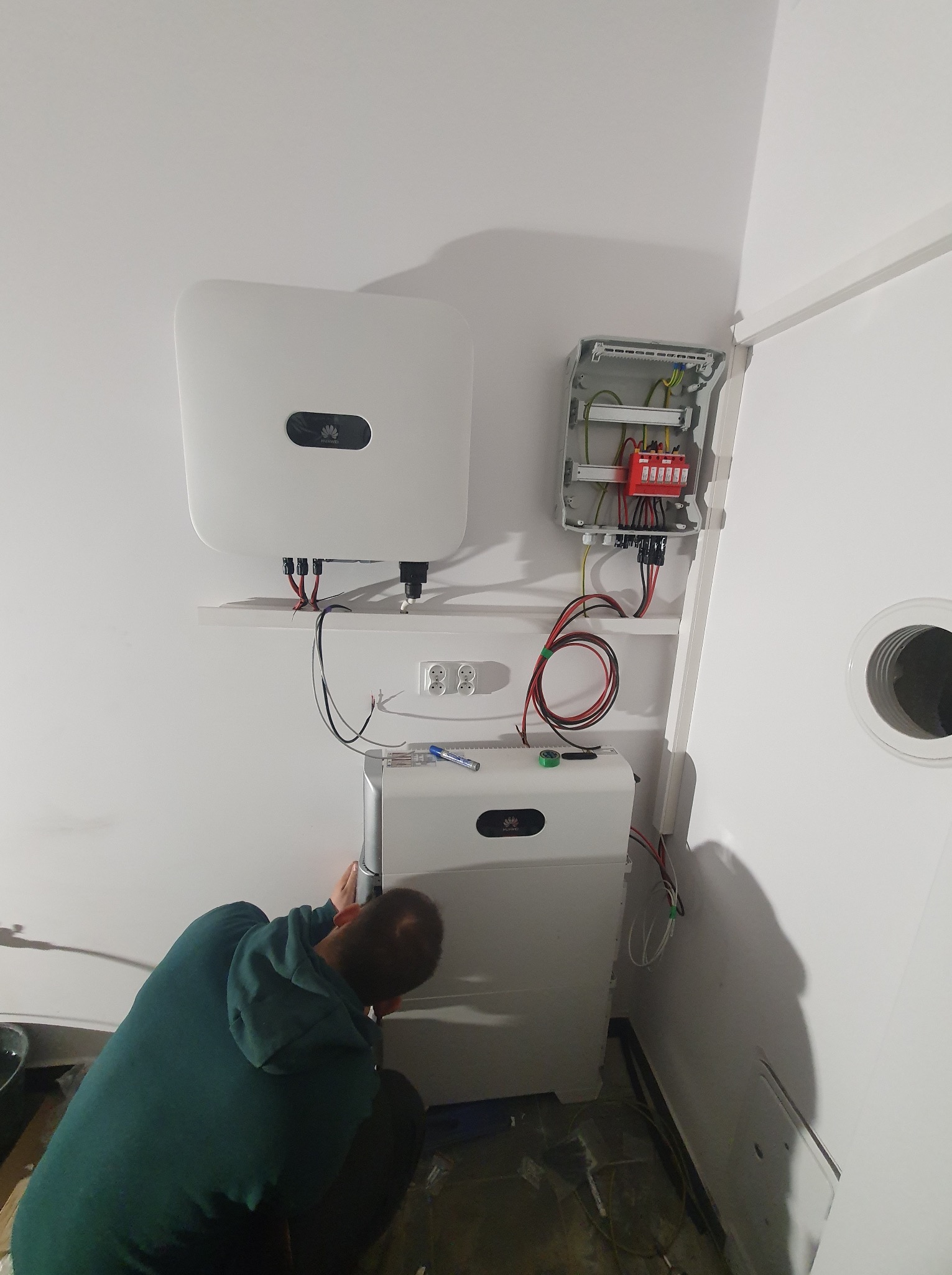 Instalacja paneli fotowoltaicznych w Białymstoku: monter w trakcie podłączania inwertera i akumulatora do rozdzielnicy. Widoczne kable i urządzenia.