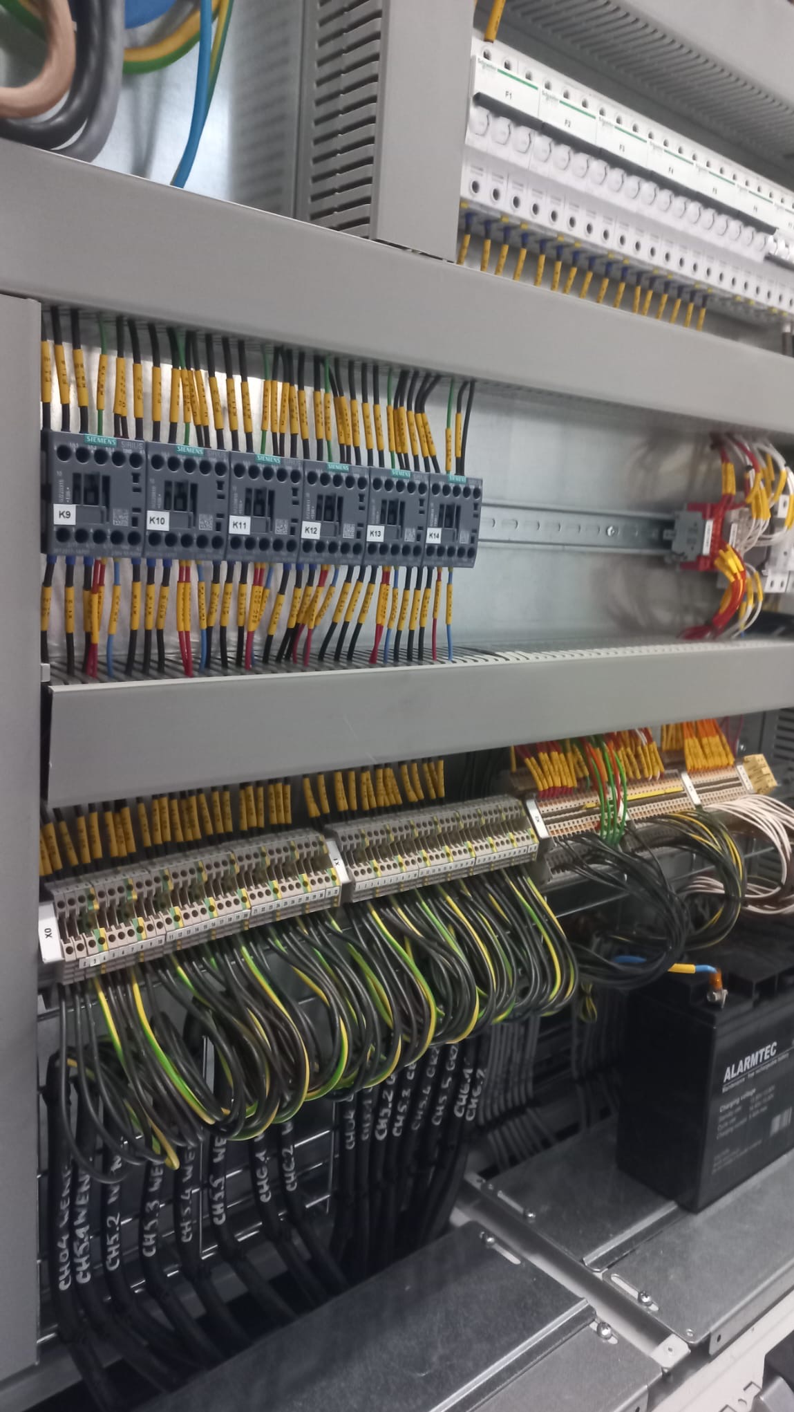 Rozdzielnica elektryczna z precyzyjnie oznaczonymi przewodami i modułami Siemens K9-K14, widoczne kable z opisami, bateria alarmowa Alarmtec.