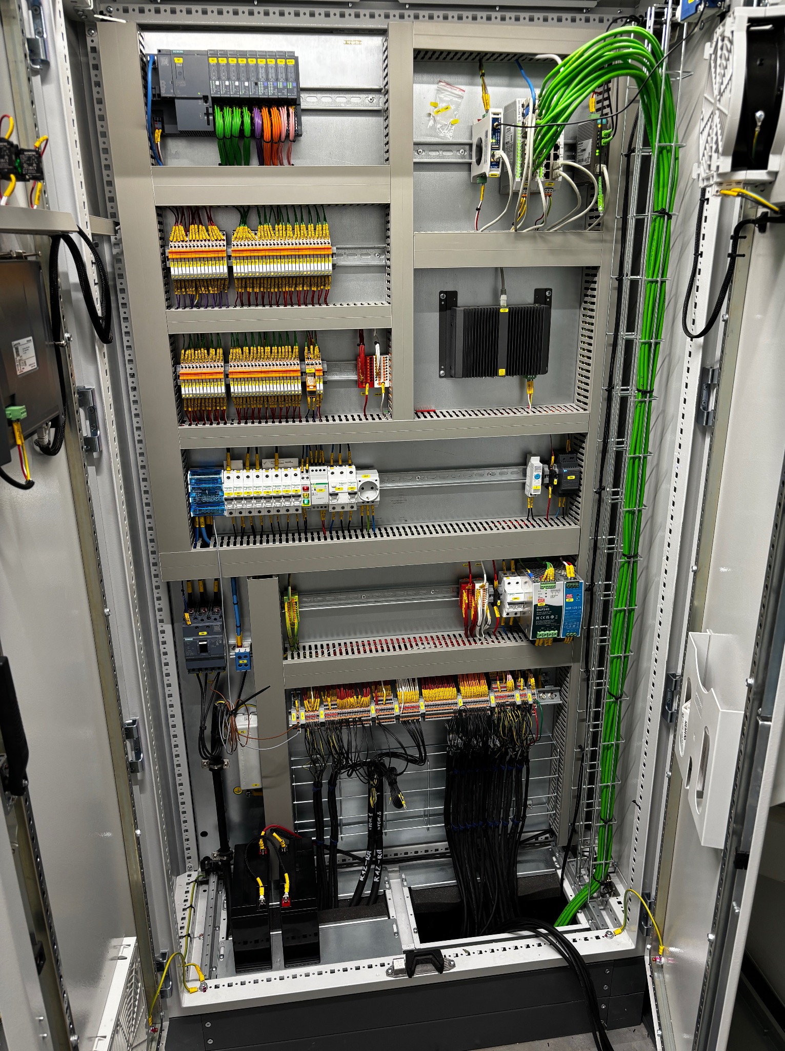 Otwarta szafa sterownicza z modułami, okablowaniem oznaczonym kolorami i zabezpieczeniami. Uporządkowany układ przewodów wewnątrz szafy elektrycznej.