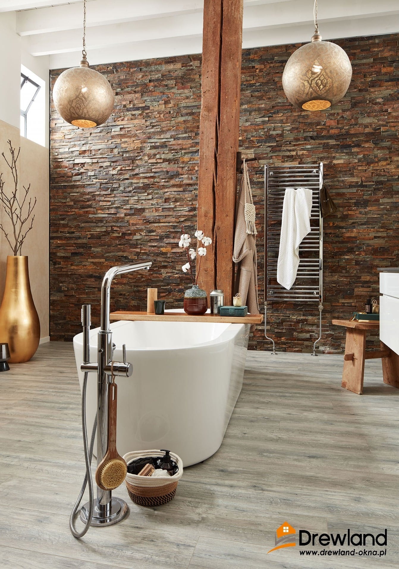 Stylowa łazienka z drewnopodobną podłogą, kamienną ścianą, wolnostojącą wanną i dekoracyjnymi lampami wiszącymi.