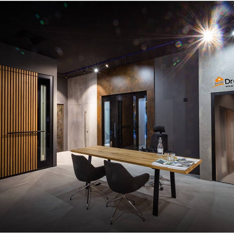 Wnętrze biura z drewnianym stołem i krzesłami, w tle zabudowa z drewnianych paneli i przeszklone drzwi.