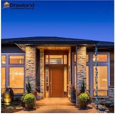 Eleganckie wejście do domu z drewnianymi drzwiami, oświetlone ciepłym światłem, z widocznymi roletami w oknach i dekoracyjnymi kolumnami z kamienia.