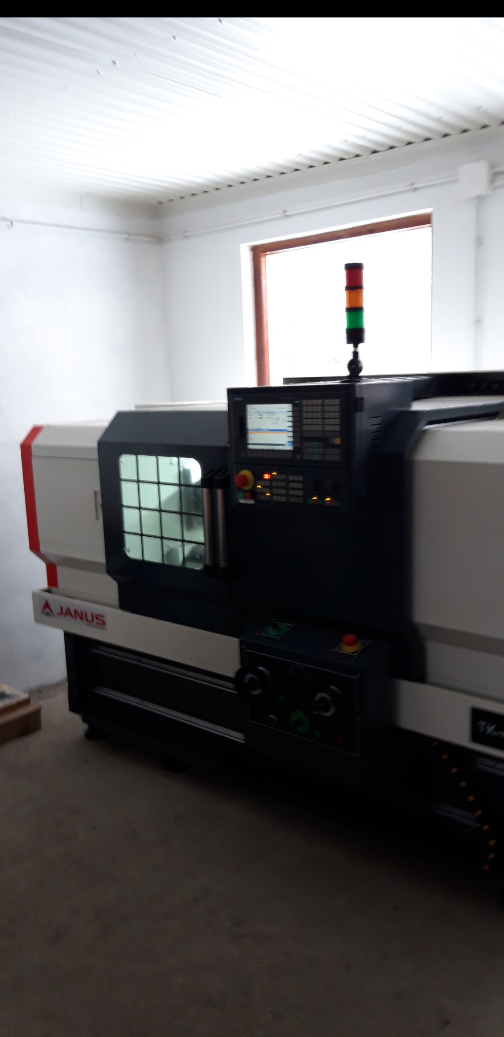 Nowoczesna tokarka CNC marki Janus w hali produkcyjnej, z widocznym panelem sterowania i sygnalizacją świetlną.