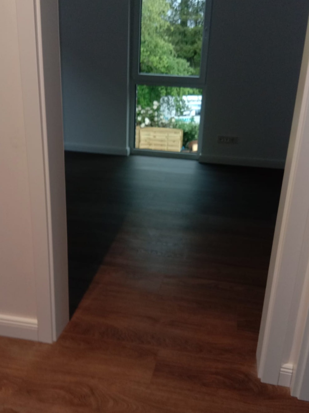 Ukończone układanie paneli podłogowych w pokoju, widok zza futryny, z oknem w tle.