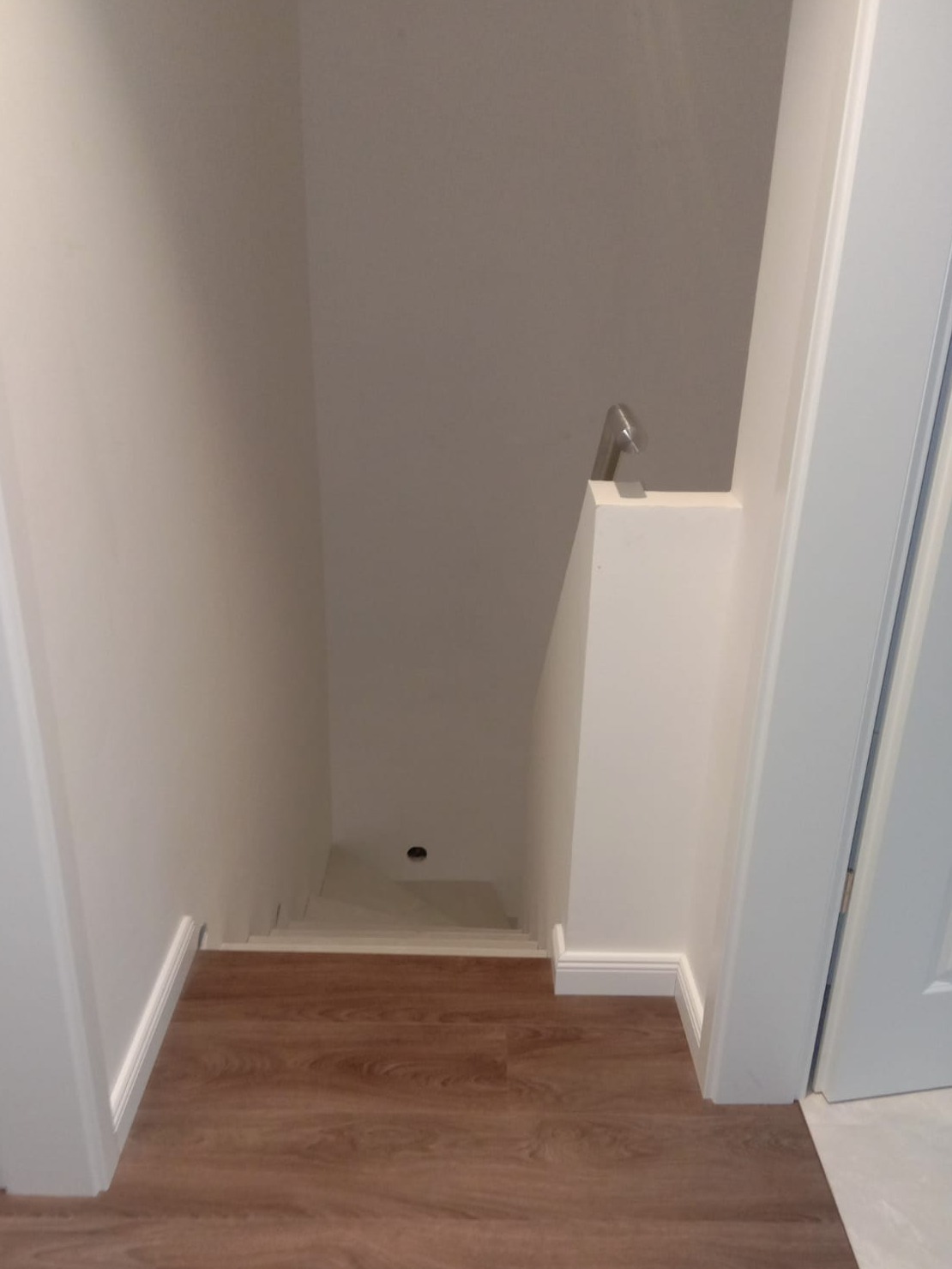 Widok z góry na schody w dół, z drewnopodobną podłogą laminowaną, białymi ścianami i poręczą ze stali nierdzewnej.