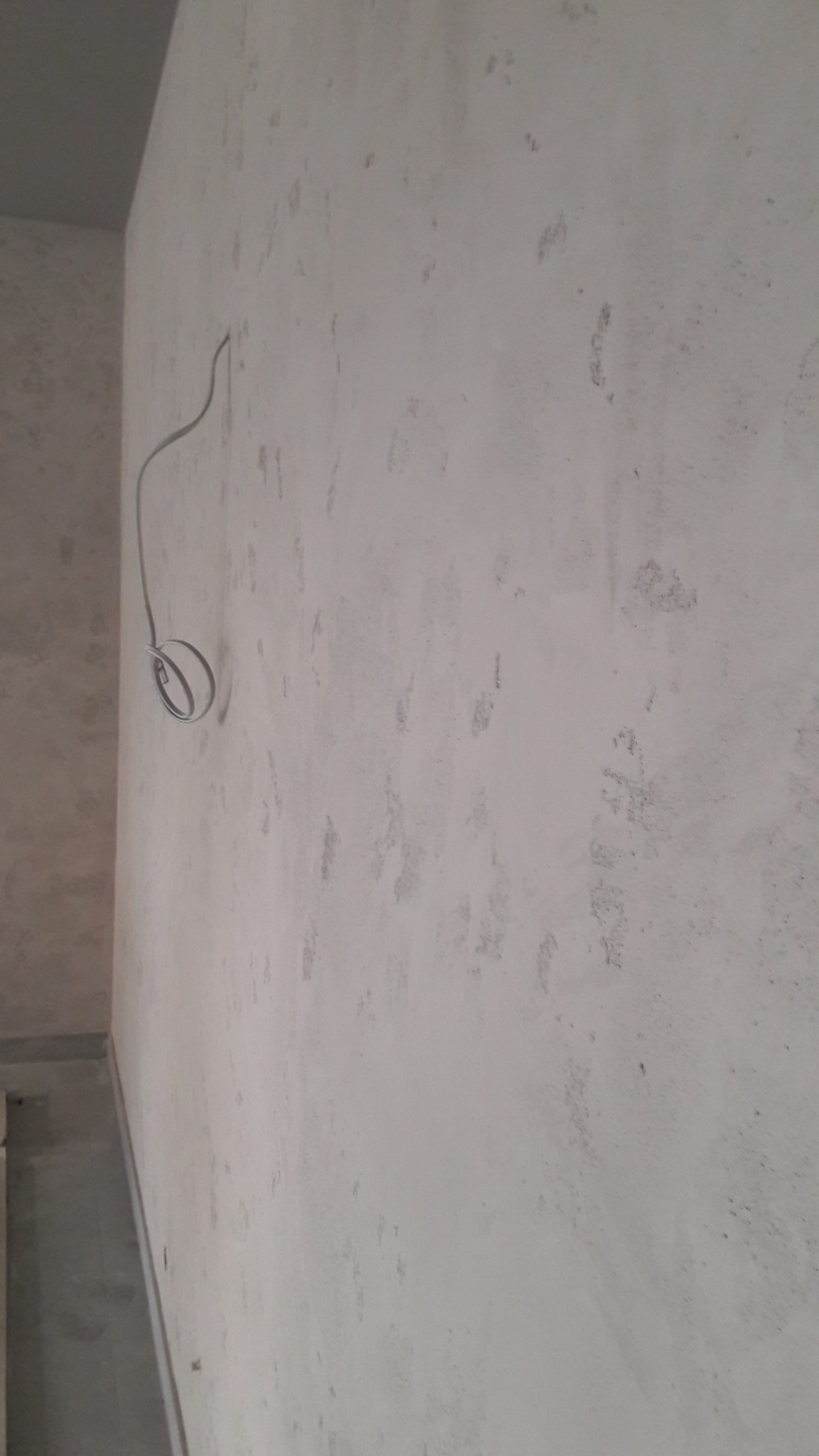 Ściana w trakcie przygotowania do nałożenia gładzi, widoczne ślady po poprzednich warstwach i wystający kabel elektryczny.