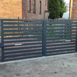 PepoAutomatyka - Nowoczesna, pozioma brama wjazdowa z automatyką, widoczna osoba w tle, brama w kolorze grafitowym, na posesji z ceglanym budynkiem i betonowym ogrodzeniem.