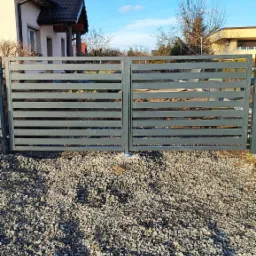 Nowoczesna brama wjazdowa z poziomych, szarych profili stalowych, zamontowana na posesji z domem i wysypanym kamieniem podłożem, błękitne niebo z chmurami w tle.