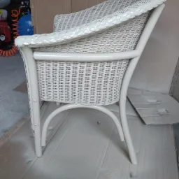 Białe, wiklinowe krzesło ogrodowe po malowaniu, z widocznymi śladami farby na kartonie zabezpieczającym podłoże.