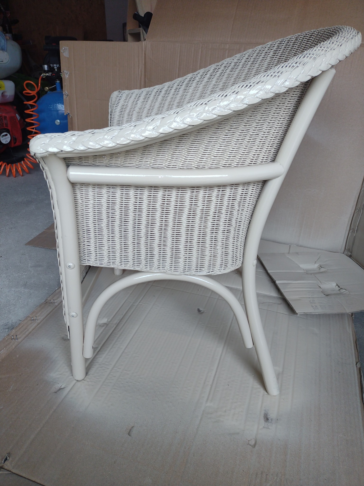 Białe, wiklinowe krzesło ogrodowe po malowaniu, z widocznymi śladami farby na kartonie zabezpieczającym podłoże.