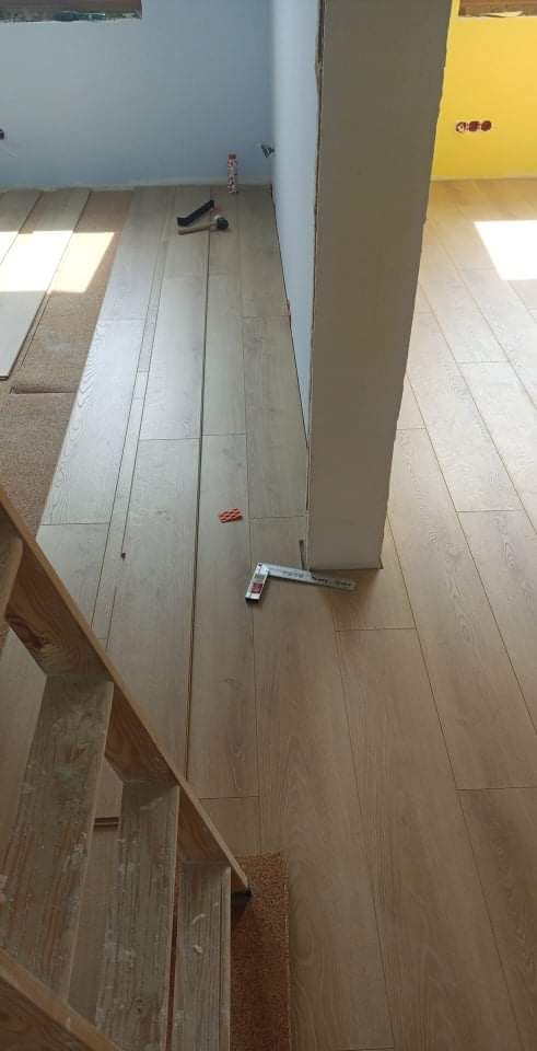 Montaż paneli podłogowych w Warszawie, widoczne narzędzia pomiarowe i fragment schodów, podkład pod panele częściowo widoczny.