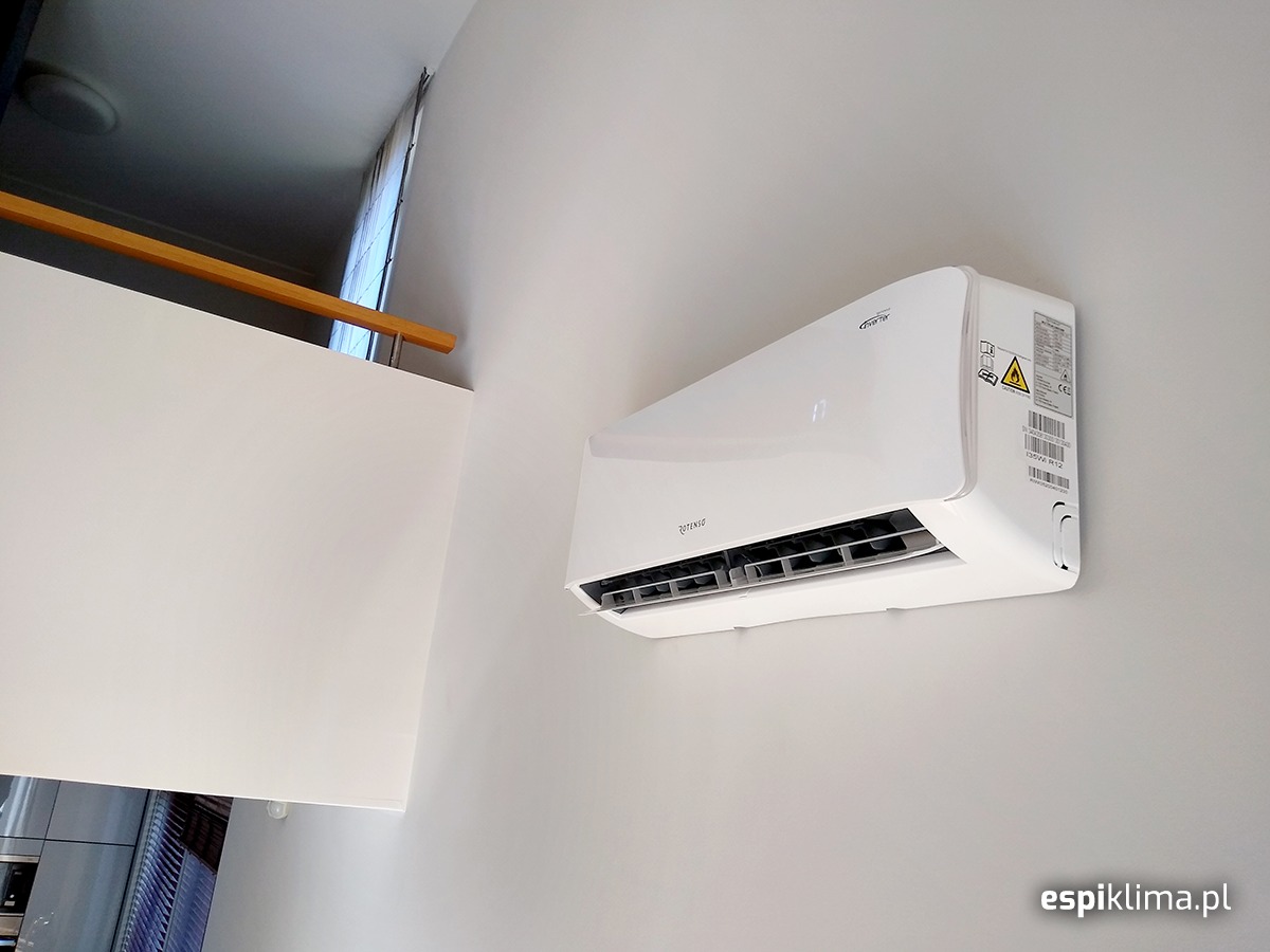 Biały klimatyzator Rotenso zamontowany na ścianie w jasnym wnętrzu domu, widoczne elementy wykończenia i balustrada.