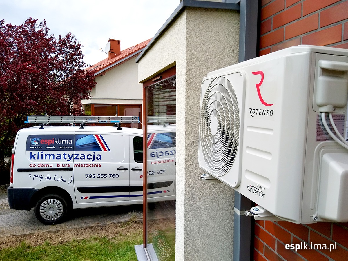 Zewnętrzna jednostka klimatyzatora Rotenso zamontowana na ceglanej ścianie budynku, z widocznym samochodem serwisowym firmy Espiklima w tle.