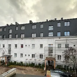 Nadbudowa budynku z elementami konstrukcji szkieletowej drewnianej, widok z zewnątrz, szare niebo, część elewacji w rusztowaniach.