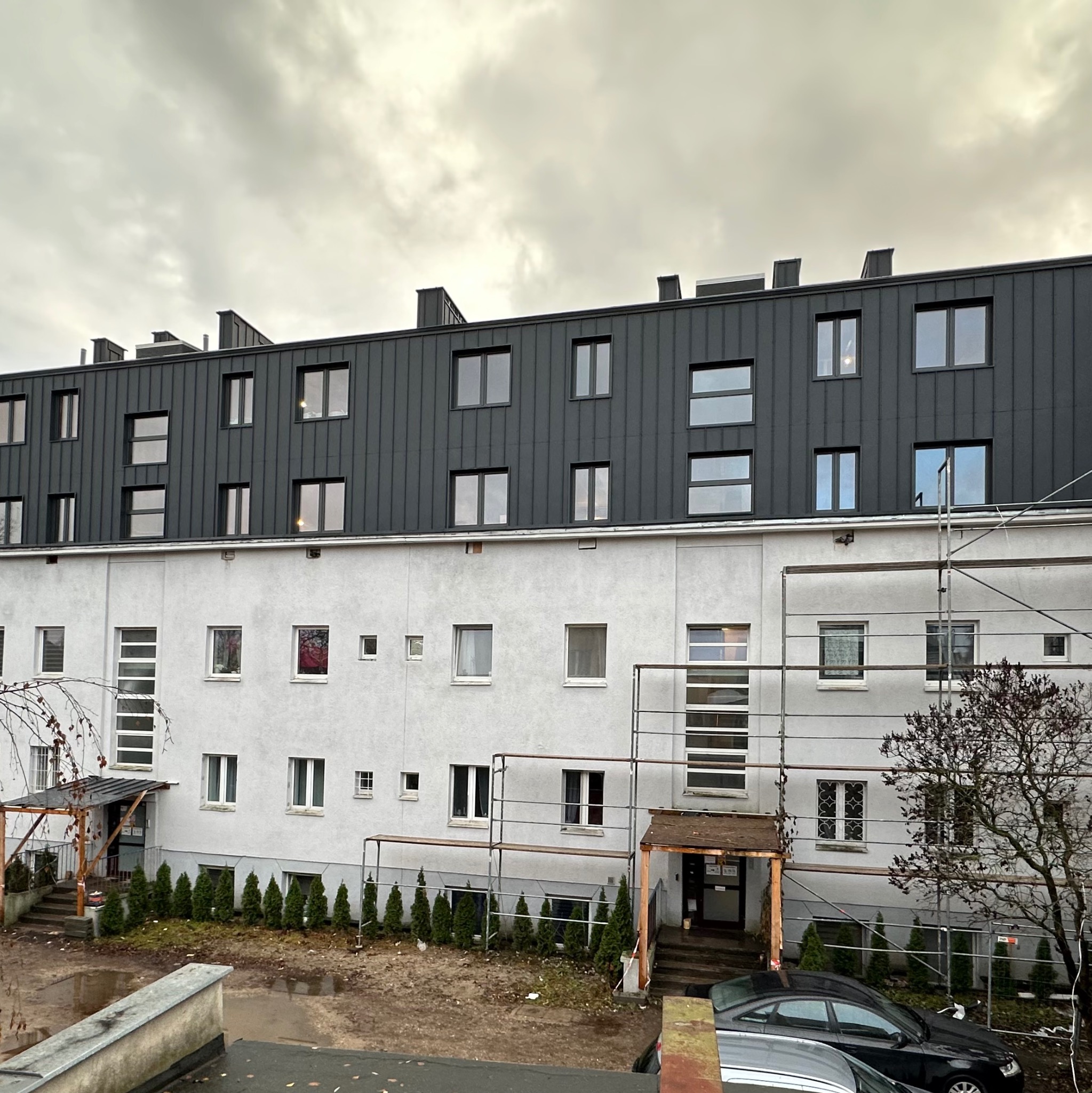 Nadbudowa budynku z elementami konstrukcji szkieletowej drewnianej, widok z zewnątrz, szare niebo, część elewacji w rusztowaniach.