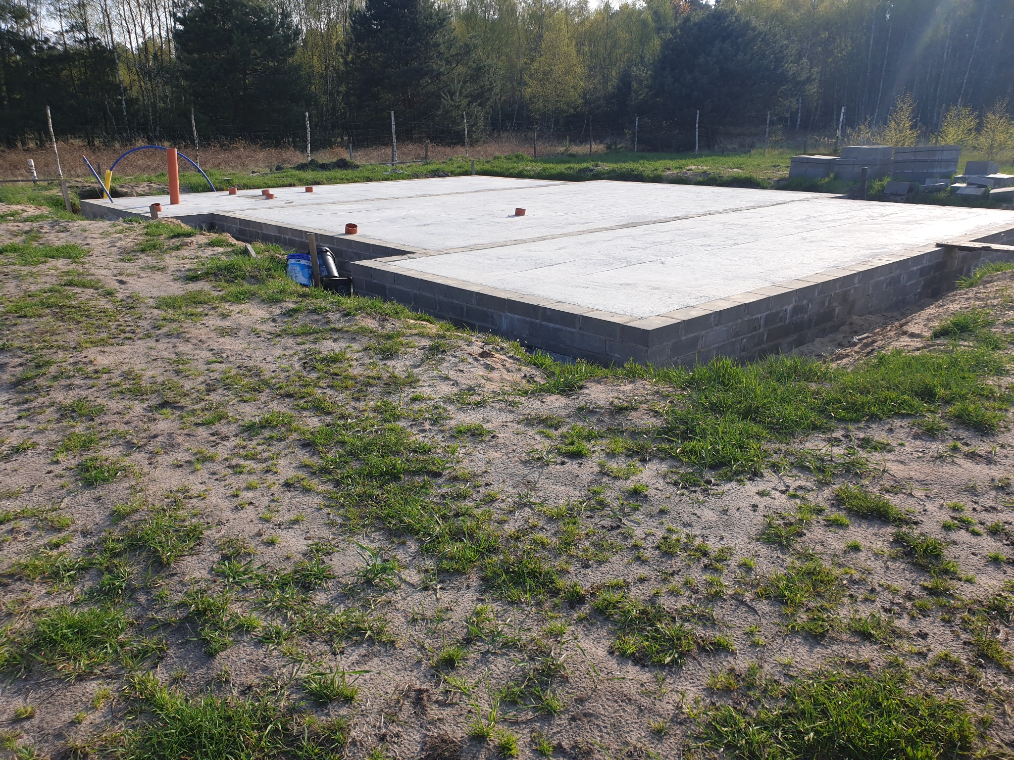 Przygotowany fundament pod budowę domu w Zduńskiej Woli, widoczne bloczki fundamentowe, betonowa płyta oraz wystające rury instalacyjne.