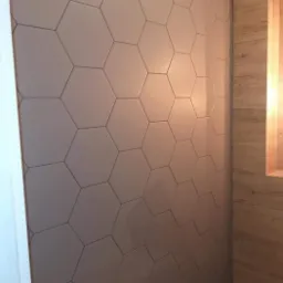 Ściana wyłożona szarymi, heksagonalnymi płytkami ceramicznymi, sąsiadująca z drewnianą okładziną z wnęką.