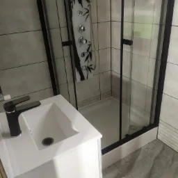 Nowoczesna łazienka z kabiną prysznicową z czarnymi ramami i panelem z motywem bambusa, biała umywalka z czarną baterią, szare płytki podłogowe imitujące marmur.