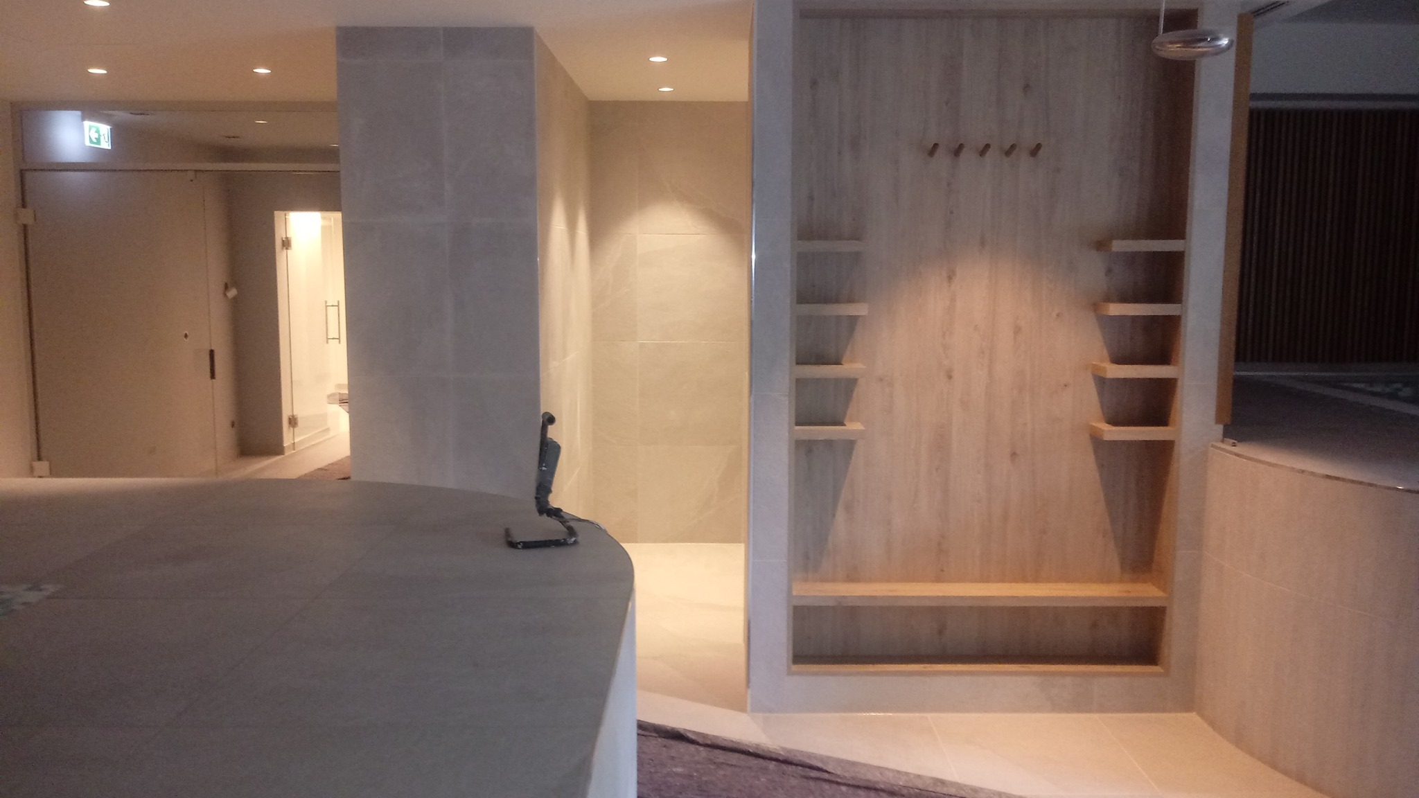 Nowoczesna łazienka w Gdańsku z jasnymi płytkami i drewnianymi elementami zabudowy, widok na kabinę prysznicową i półki.