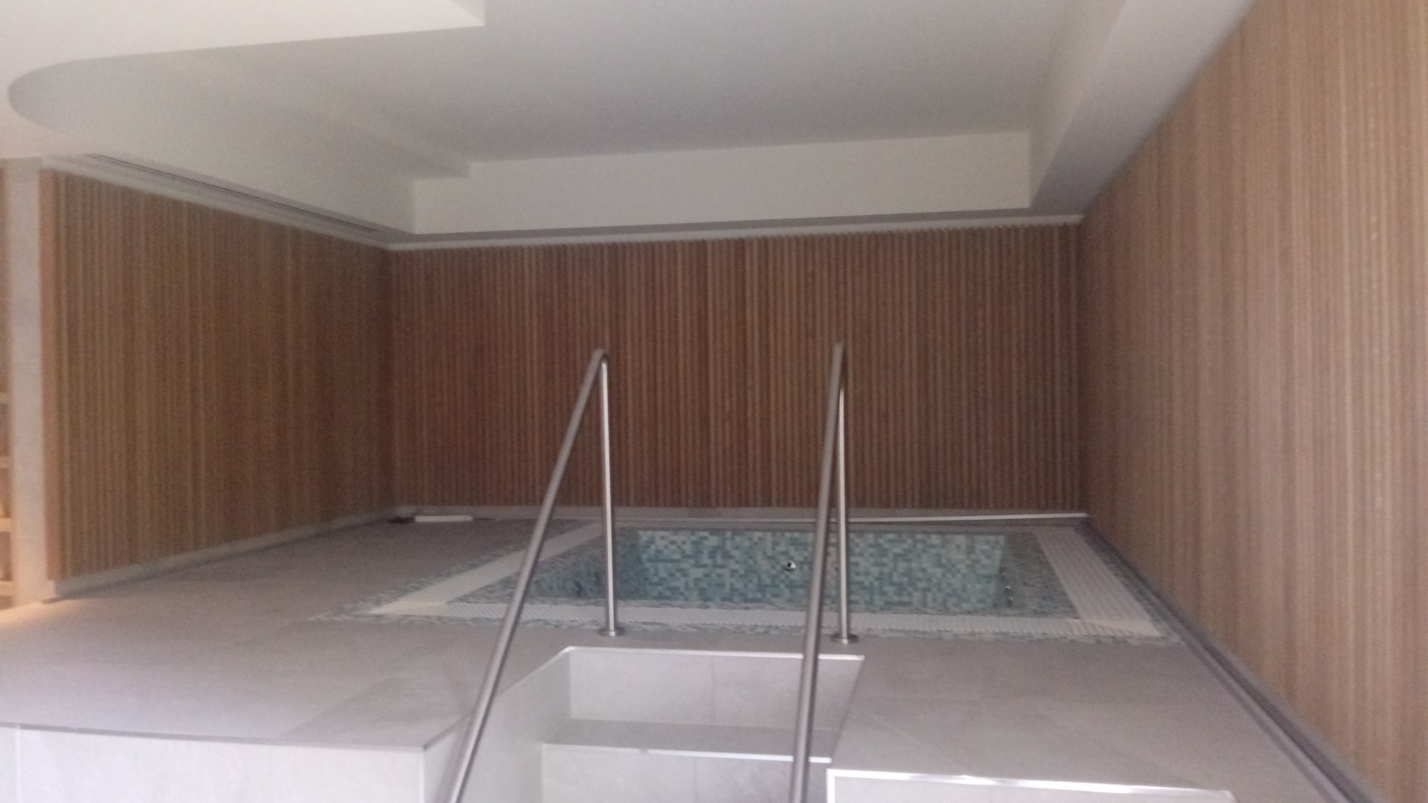 Nowoczesna łazienka z drewnianą boazerią i małym basenem wyłożonym mozaiką, widok z góry schodów wejściowych.