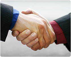 Uścisk dłoni dwóch mężczyzn w garniturach, symbolizujący porozumienie i współpracę, z lekkim rozmyciem tła.