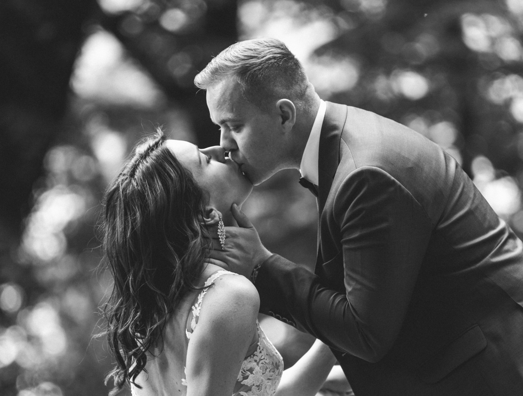 Czarno-białe zdjęcie całującej się pary młodej w Lesznie, panna młoda z długimi kolczykami i koronkową suknią, pan młody w garniturze.