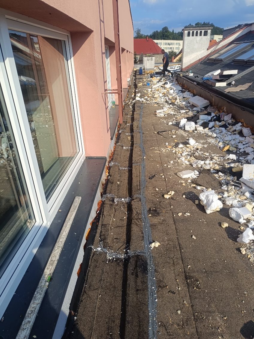 Demontaż starego dachu z papy bitumicznej, widoczne resztki izolacji termicznej i pracownik w tle.