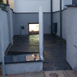 Mój Market Avetik Vanetsyan - Ułożona, ciemna kostka brukowa na podwórku między budynkami, widoczne studzienki kanalizacyjne i fragment chodnika z czerwonej kostki.