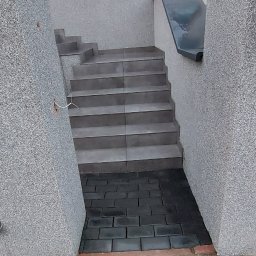 Mój Market Avetik Vanetsyan - Zewnętrzne schody wyłożone szarymi płytkami prowadzące od ciemnej kostki brukowej do czerwonej kostki, ściany wykończone szarym tynkiem strukturalnym, widoczne przewody elektryczne.