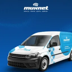 Biały samochód dostawczy z niebieskimi akcentami i logo firmy Muxnet oferującej telewizję, internet, alarmy i elektrykę, zaparkowany na niebieskim tle.