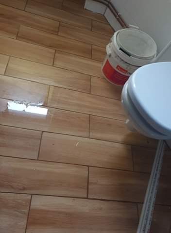Ułożone płytki podłogowe imitujące drewno w łazience, widoczne wiadro z farbą i fragment toalety.