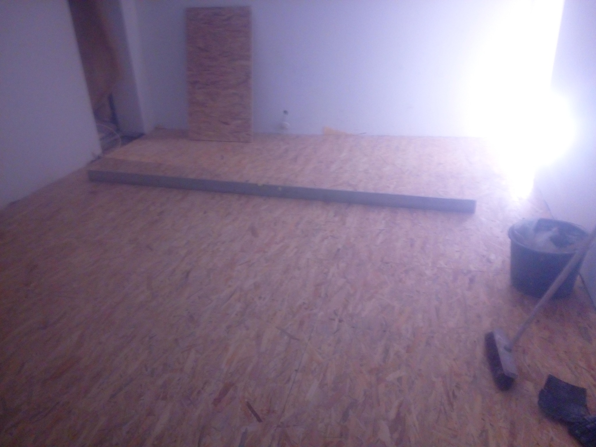 Przygotowanie podłoża z płyt OSB pod przyszłą podłogę w pomieszczeniu, widoczna listwa poziomująca, wiadro i szczotka.