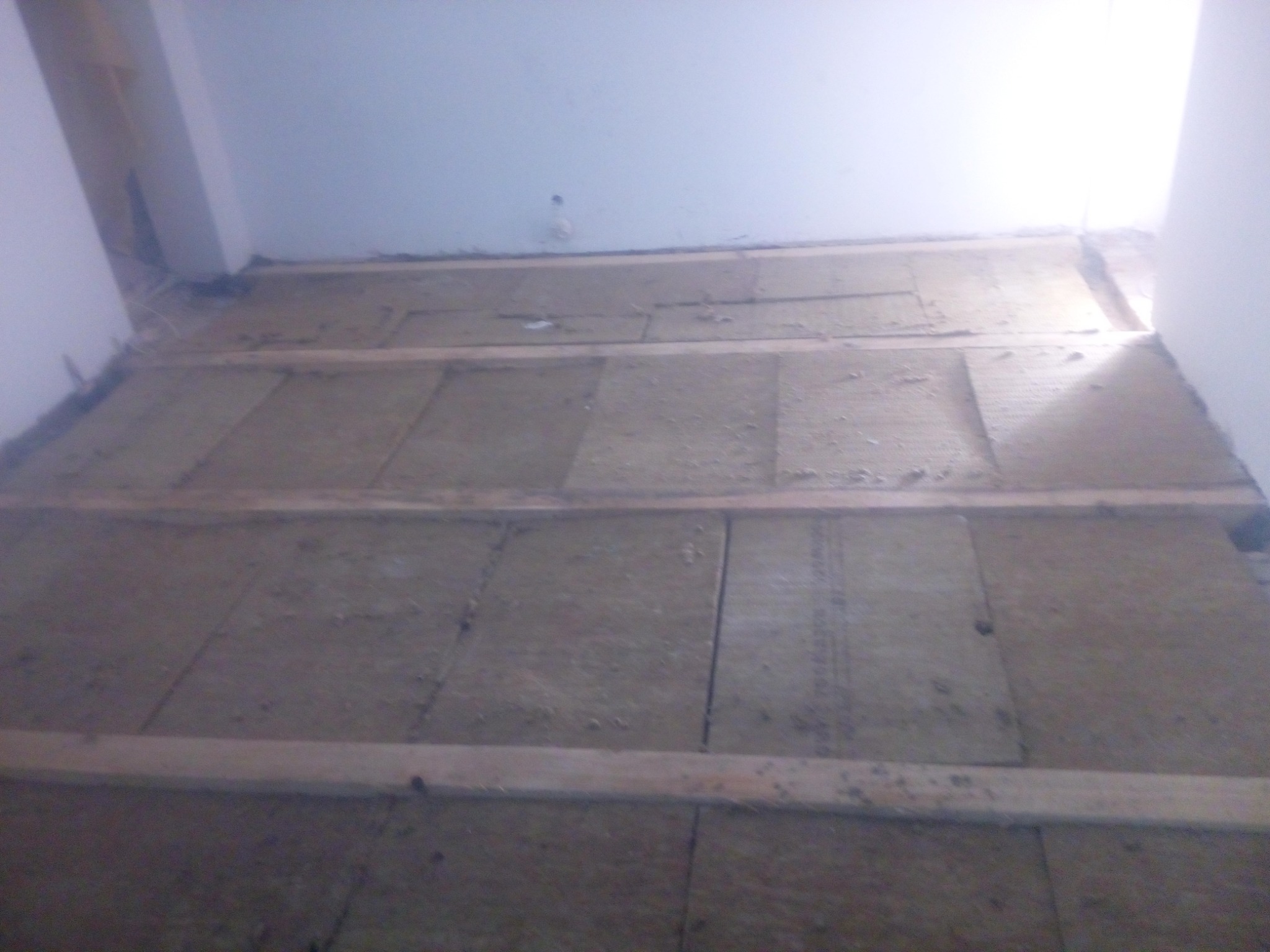 Płyty izolacyjne z wełny mineralnej ułożone między drewnianymi legarami na poddaszu, widoczne ślady montażu i niedoskonałości na powierzchni izolacji.