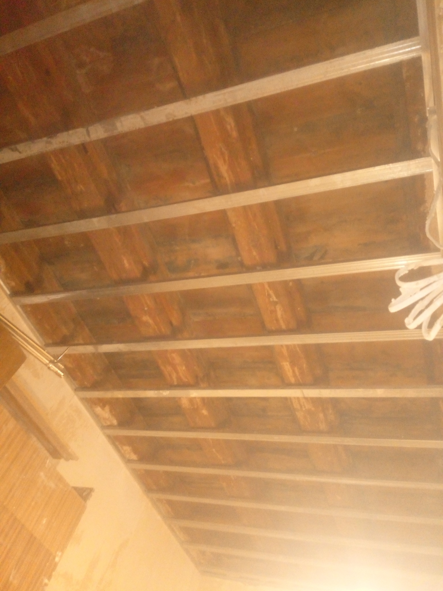 Konstrukcja podwieszanego sufitu z drewnianymi panelami, widok z dołu, metalowe profile montażowe, ślady kurzu i niedoskonałości na panelach.