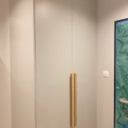 Szara szafa wnękowa z drewnianymi uchwytami, widoczny fragment zabezpieczonej ściany podczas remontu.