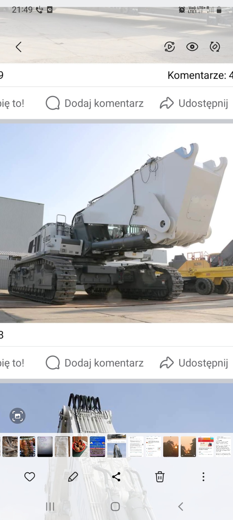 Ogromna, biała koparka gąsienicowa Liebherr 980 z łyżką o dużej pojemności, stojąca na placu budowy przy metalowym magazynie, widoczna również mniejsza żółta ładowarka.