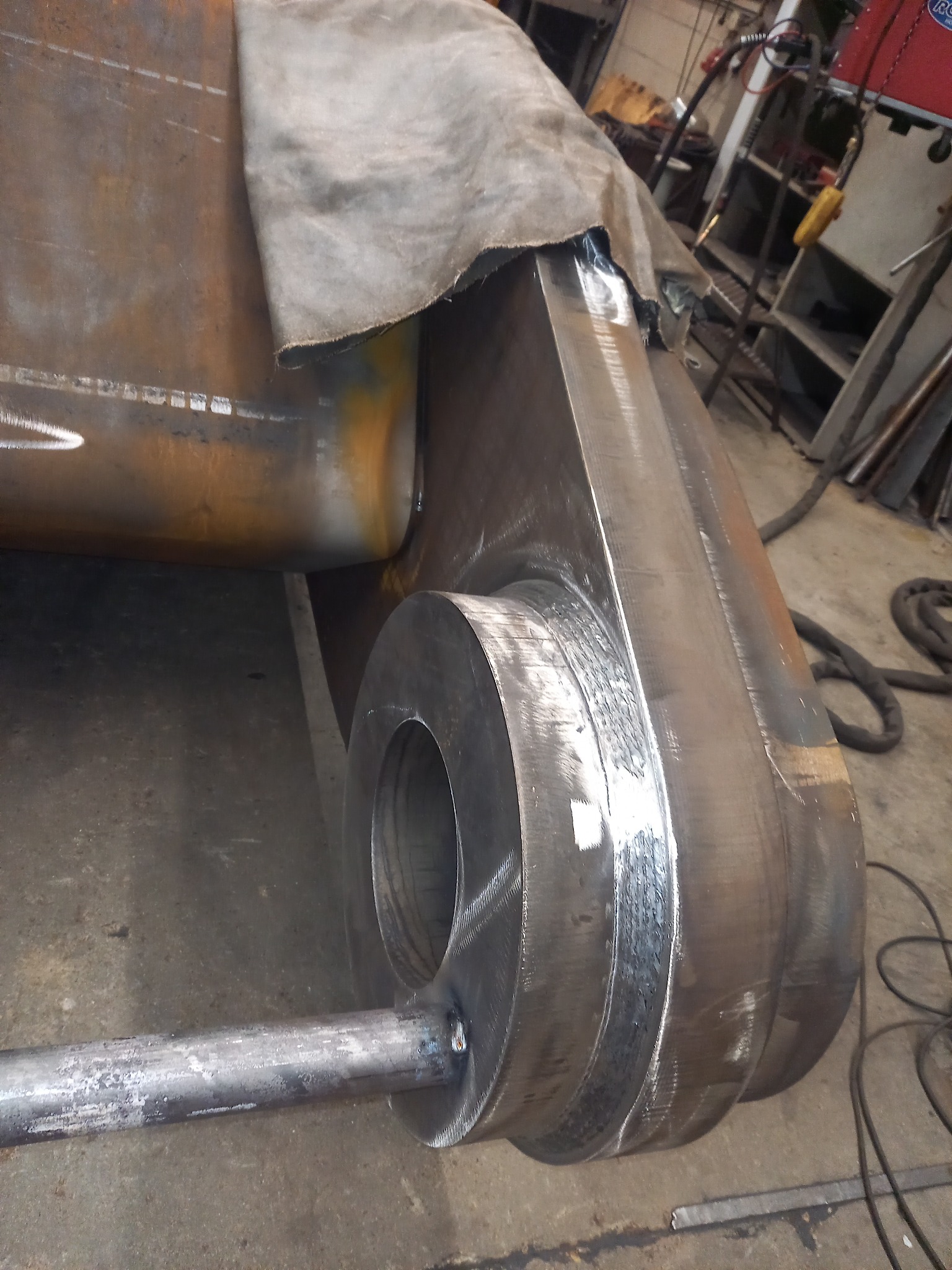 Element konstrukcyjny z grubych blach i rur, po spawaniu, widoczne ślady obróbki i szlifowania spoin, w tle warsztat.