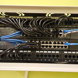 ENERGY - TELETECH CEZARY WIŚNIEWSKI - Panel krosowniczy z podłączonymi kablami sieciowymi Ethernet, część kabli spięta opaskami zaciskowymi, widoczny switch TP-Link TL-SG1024D, oznaczenia portów C5e i Cat.5e.