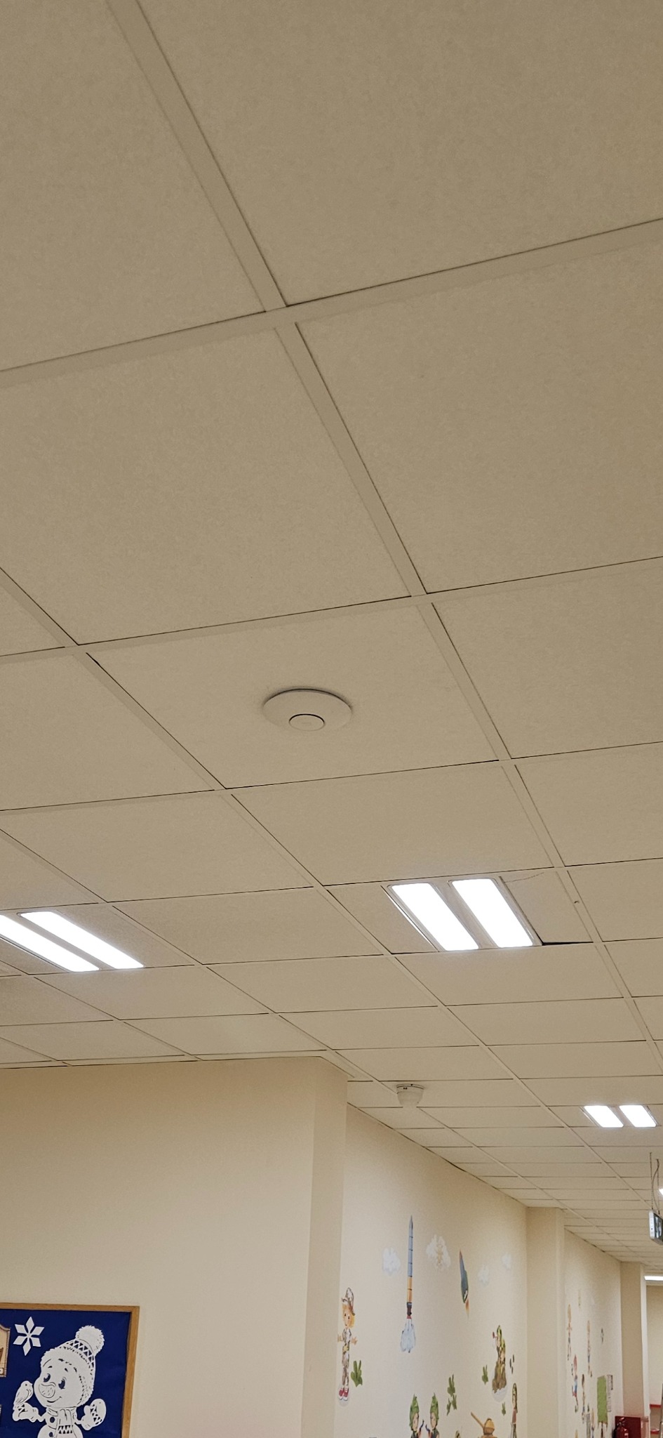 Kasetonowy sufit podwieszany z wbudowanym czujnikiem dymu i oświetleniem LED w jasnym pomieszczeniu z dekoracjami ściennymi.