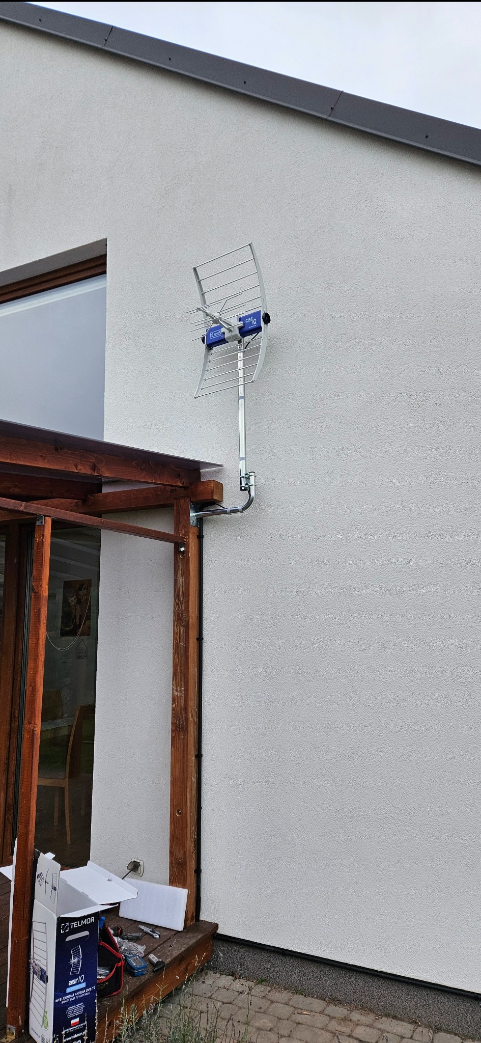 Antena DVB-T2 zamontowana na elewacji domu w Nasielsku. Widoczne kable i elementy montażowe. Obok drewniana konstrukcja z zadaszeniem.