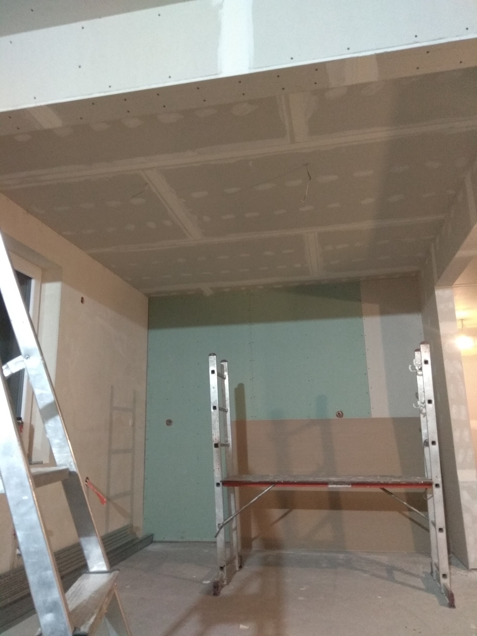 Wnętrze w trakcie montażu płyt kartonowo-gipsowych na suficie i ścianach, widoczne rusztowanie i drabina aluminiowa.