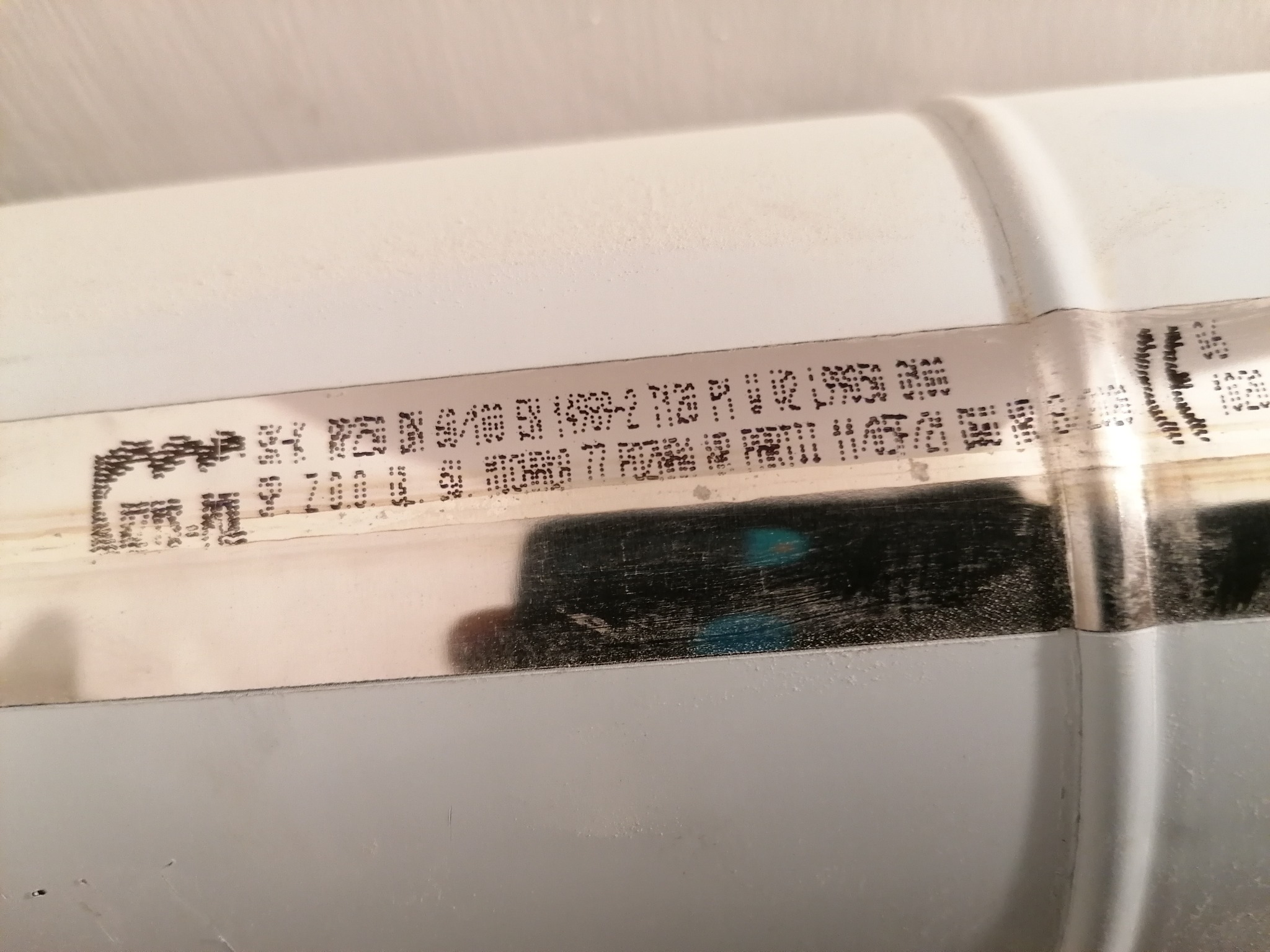 Szczegółowe ujęcie białej rury z widocznymi nadrukami technicznymi i oznaczeniami producenta, zarysowaniami i śladami użytkowania.