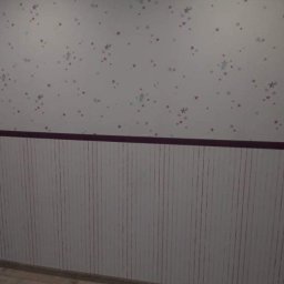 Ben-Bud - Pokój dziecięcy po odświeżeniu: Białe ściany z motywem gwiazd (czerwone i niebieskie), dolna część ściany wykończona panelami ściennymi w pionowe paski, podłoga z paneli drewnopodobnych.